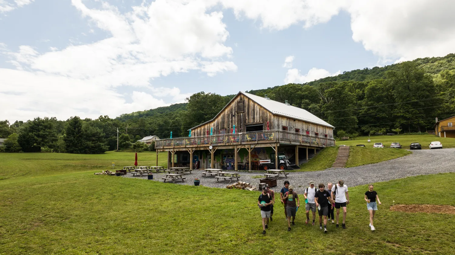 Six disc golfers make their way up a large green hill toward a large wooden barn that is now a brewery.