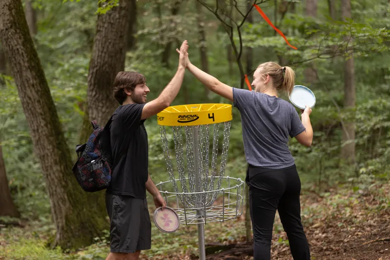 Two players high-five in front of a disc golf basket at the Locust Post Brewery course.