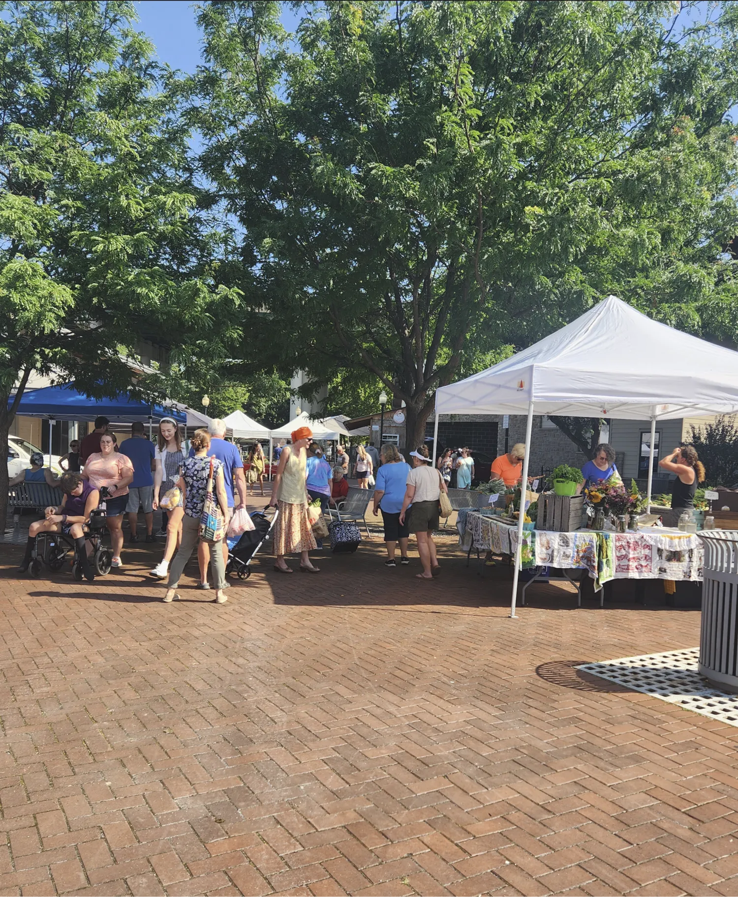 Large tents line a brick walkway and many residents and visitors walk along, shopping at the many vendor stalls.