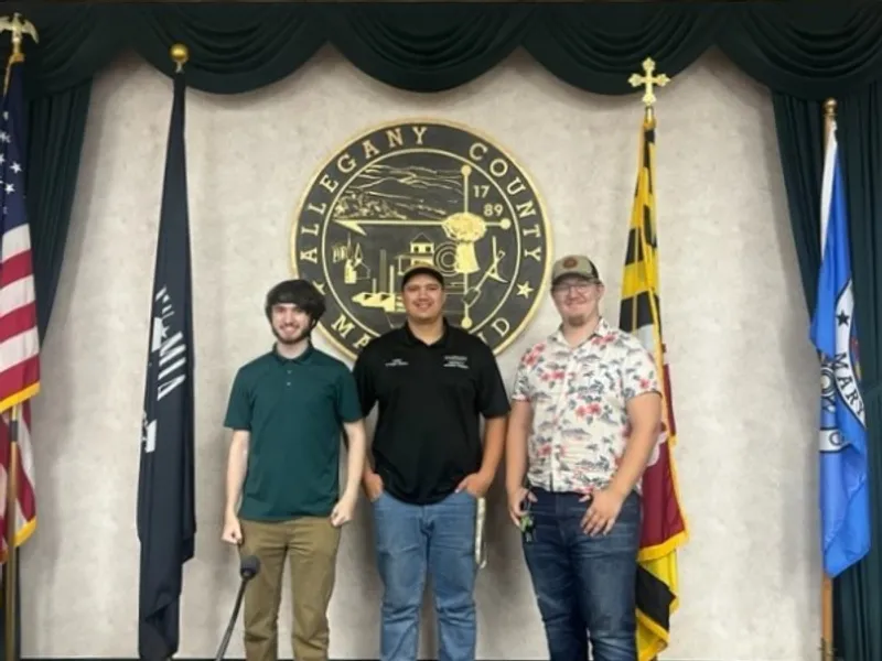 Two P-Tech interns and one supervisor stand in front of the seal of Allegany County, Maryland.