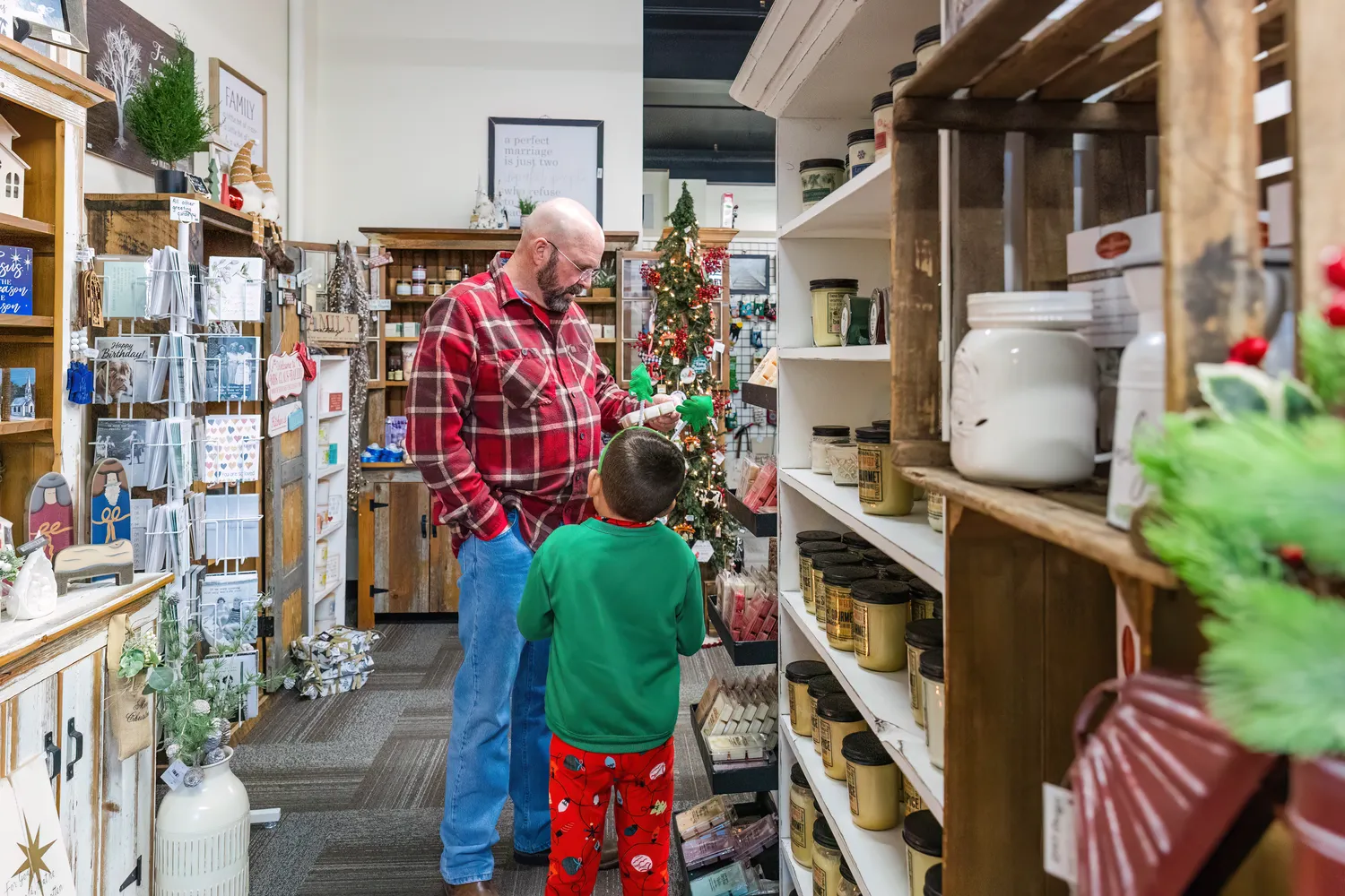 A man and a boy, dressed in holiday colors, walk down the aisle of a small business selling pottery and candles.