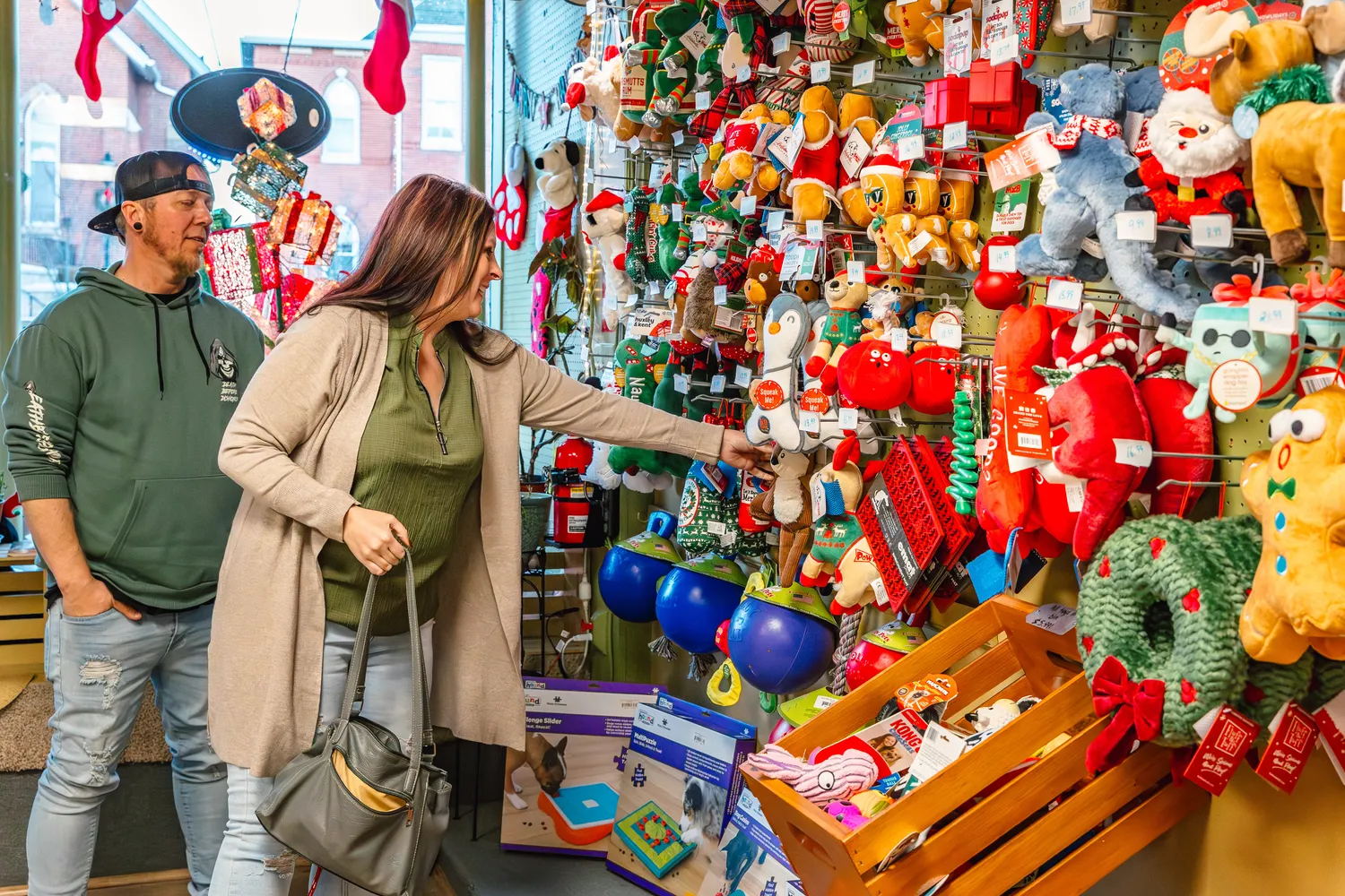 A couple shops in a colorful pet store, looking at a wall of stuffed toys.