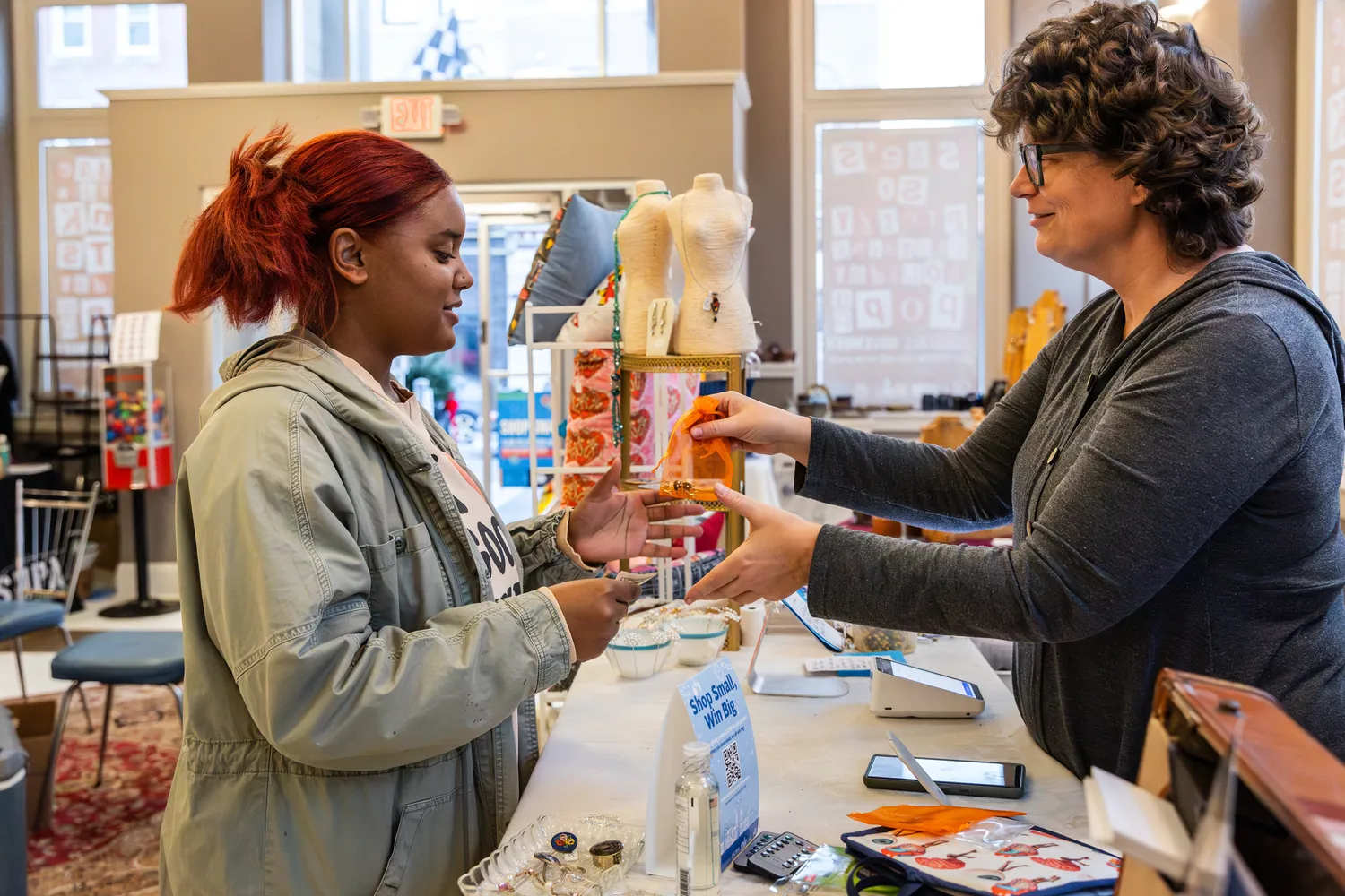 A young girl stands in front of a business counter and exchanges money with a store clerk.