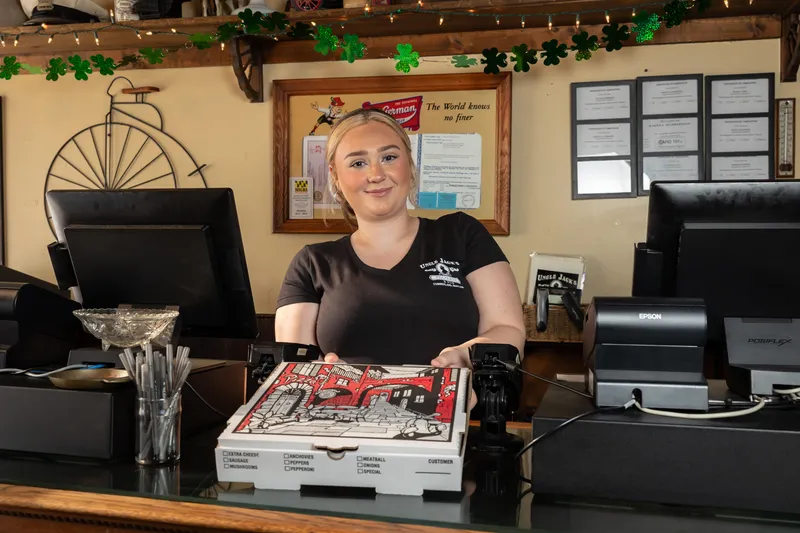 Woman with pizza boxes stands behind the counter at Uncle Jack's Pizzeria & Pub.