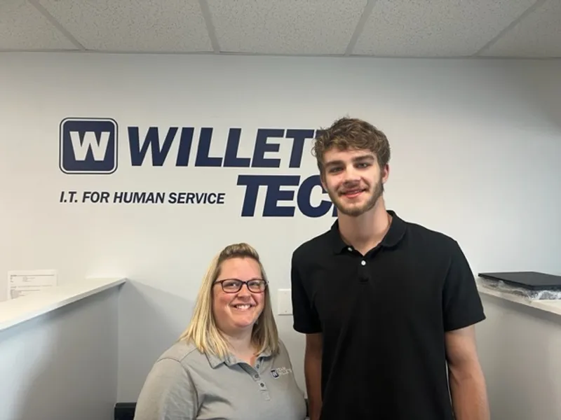 P-Tech intern and their supervisor at Willets Tech stand in front of the Willets Tech logo