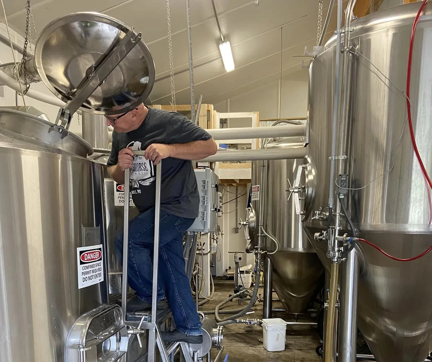 A man inspects the insides of a large silver beer brewing apparatus.