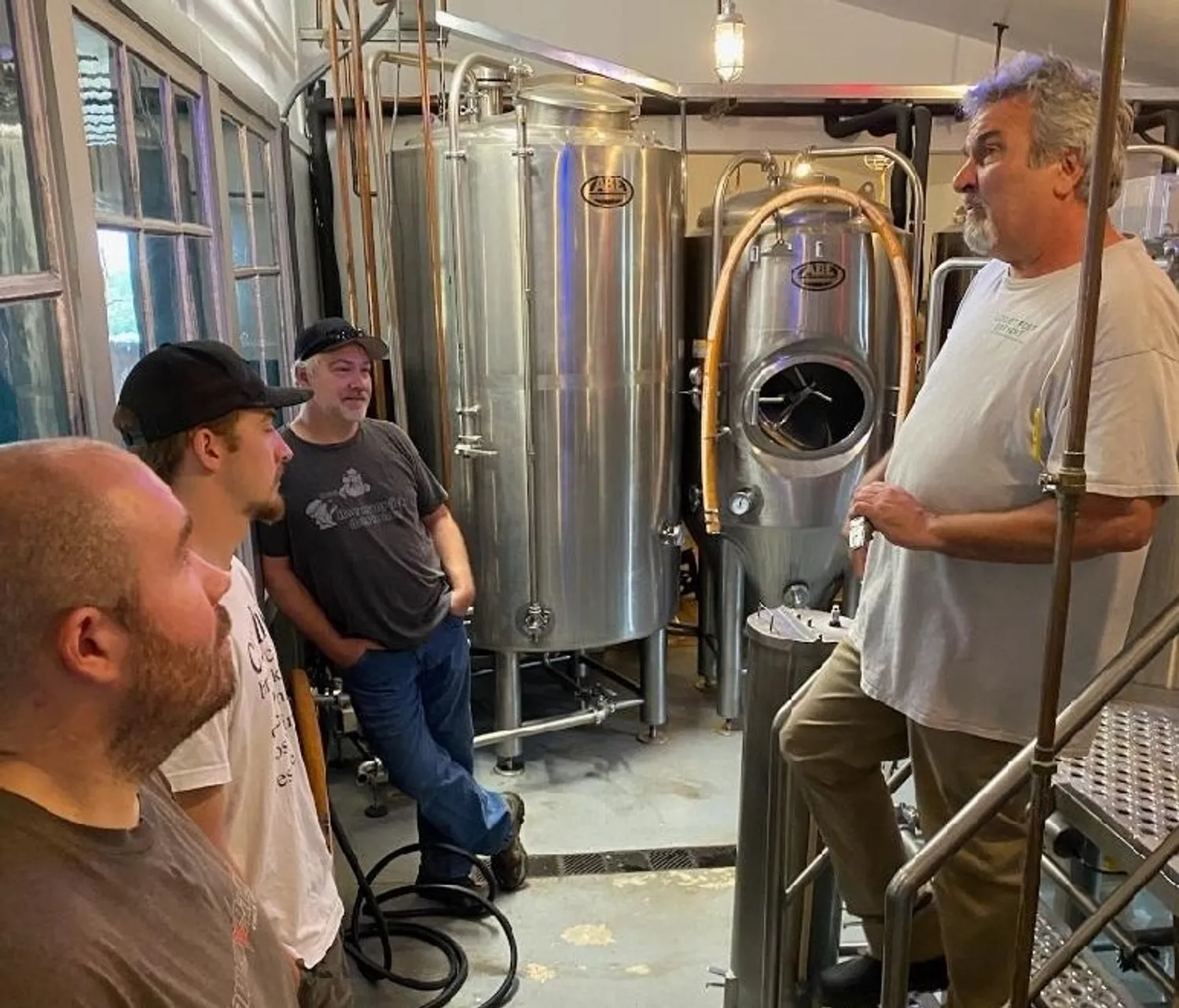 Four men stand around production beer equipment.