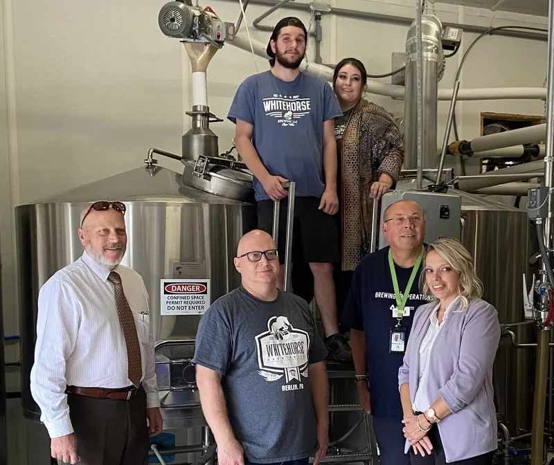 Graduates, partners, and educational staff all connected with the ACM Brewing Certification stand in a production brewing environment.