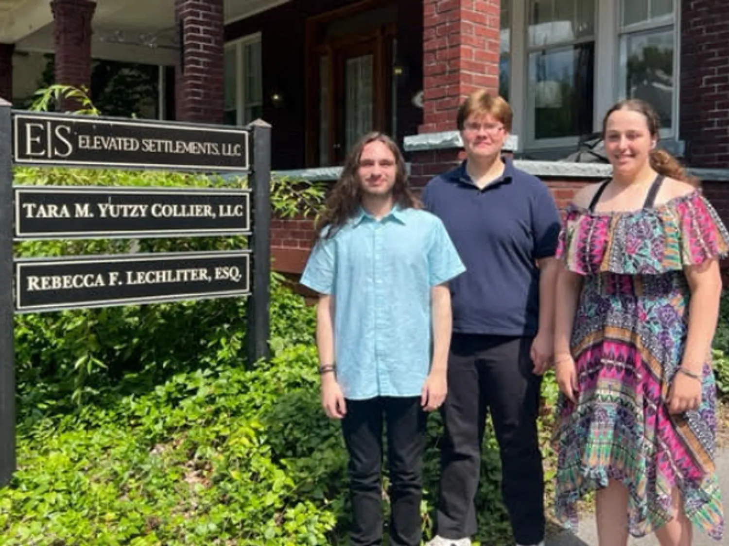 Three P-Tech interns stand outside of a brick building that hosts the offices where they interned.