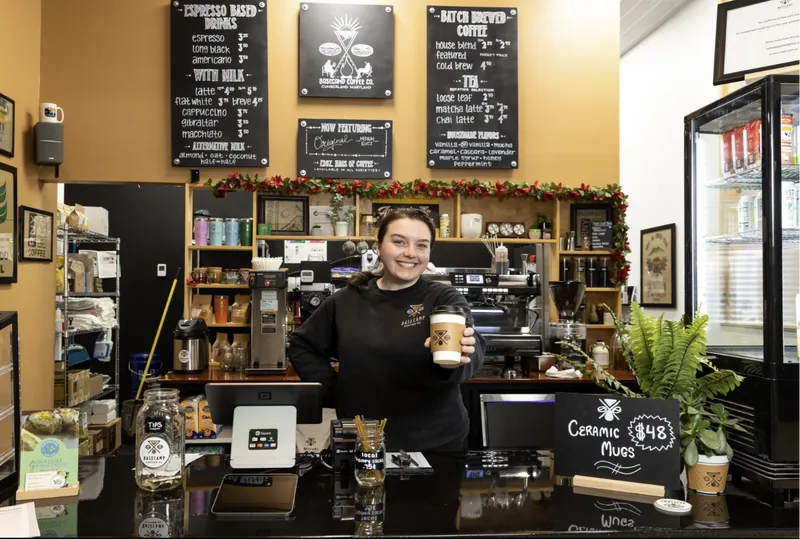 A barista hands out a cup of coffee behind the counter of Basecamp Coffee inside The Rosenbaum.
