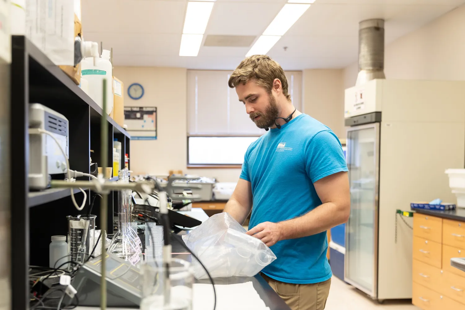 A young person wears a blue shirt and works in a lab setting.