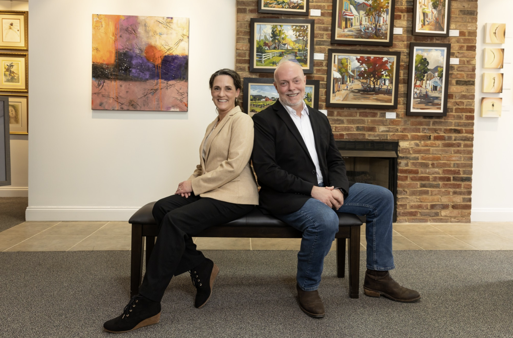 Rebecca and Thomas Ferleman sit on a bench in their art gallery